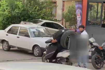 Otomobil lastiğini boynuna asan kuryenin ilginç taşıma yöntemi kameraya yansıdı